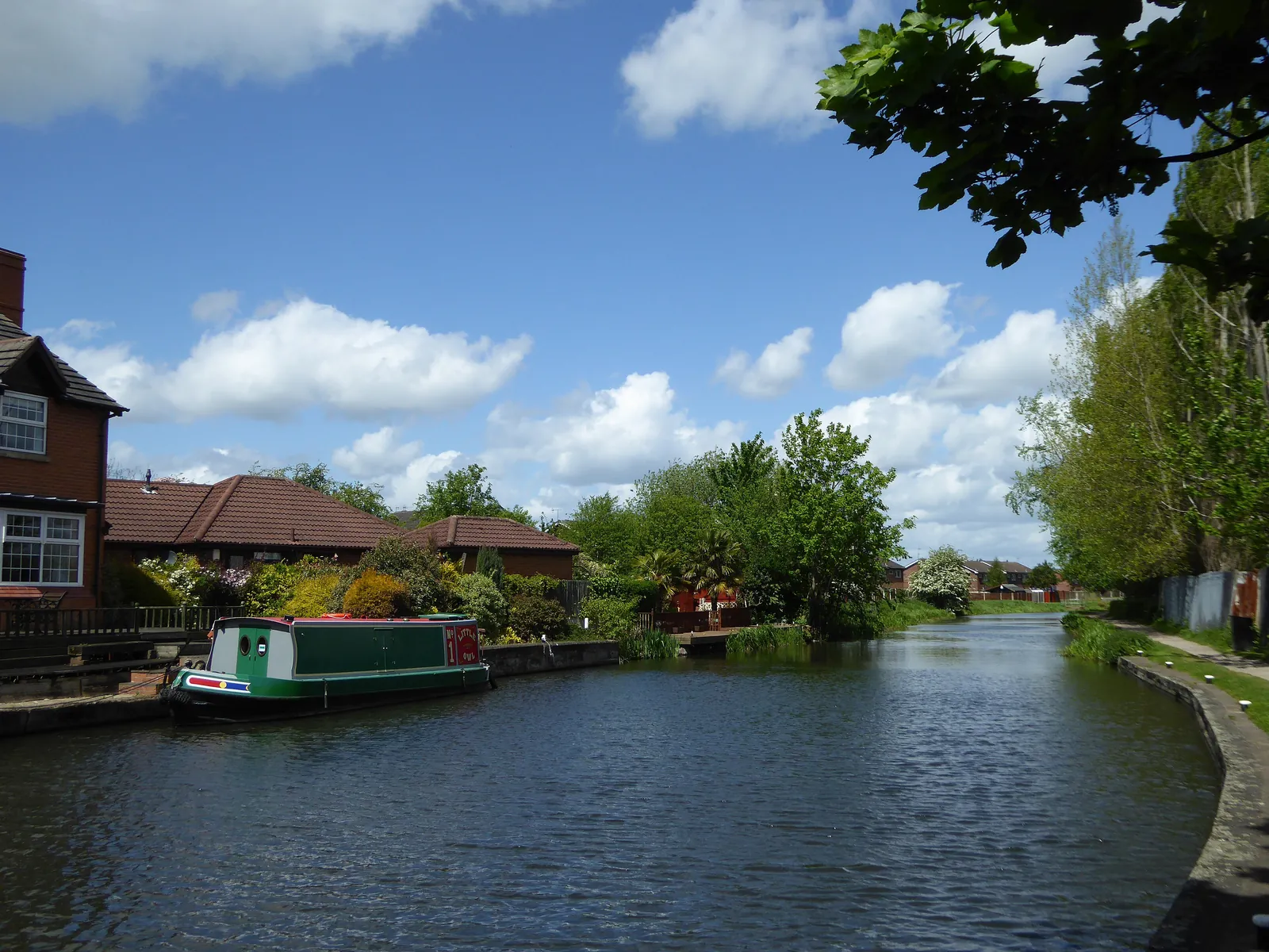 A green narrowboat moored on the Erewash Canal in Ilkeston, with houses and gardens along the bank