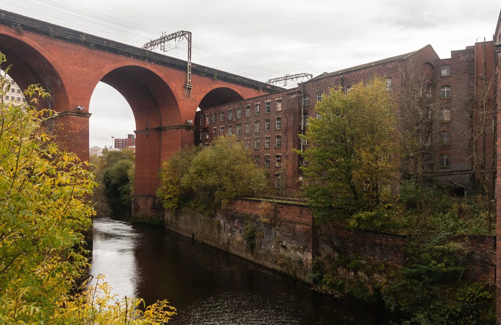 Stockport's red-brick railway viaduct arching over the River Mersey beside a tall brick mill